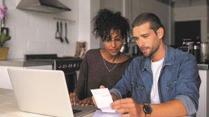Man and Woman Look at Receipt In Front Of Computer